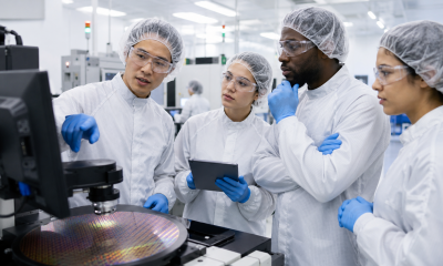 Technicians in cleanroom gear review wafer inspection equipment in a semiconductor manufacturing training environment.