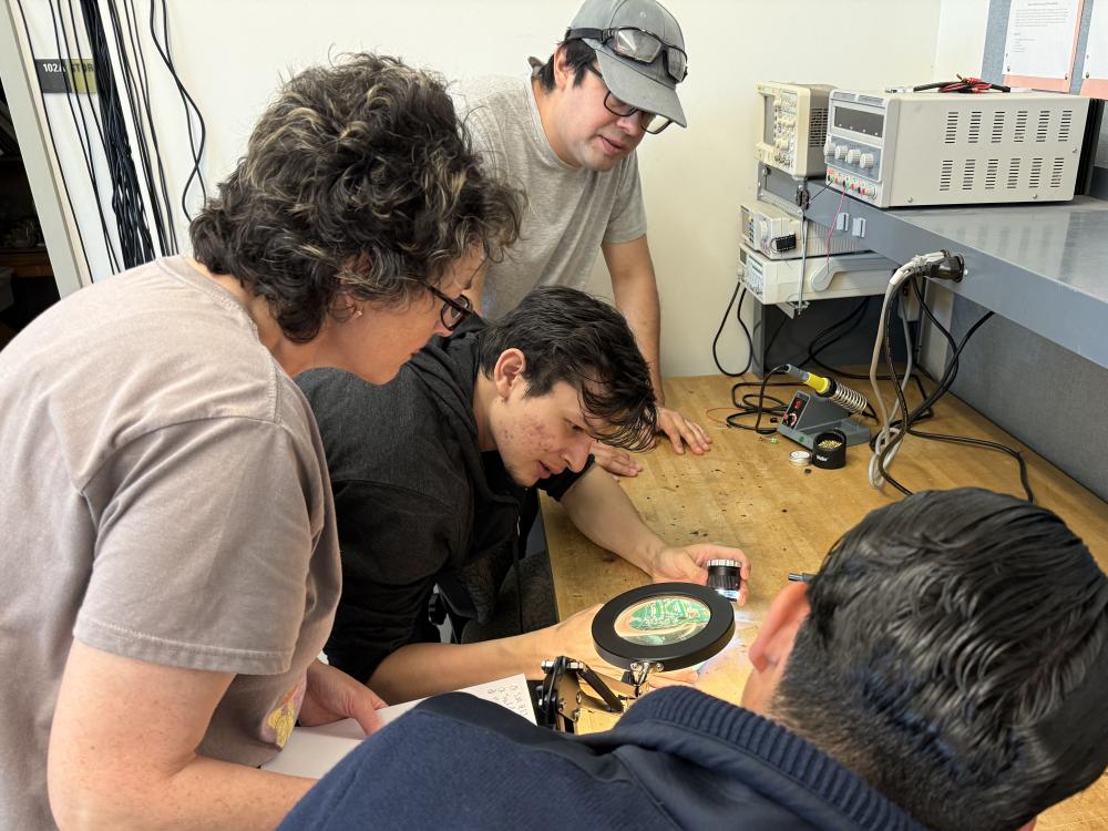 Student and teacher looking at a circuit board through a magnifying glass