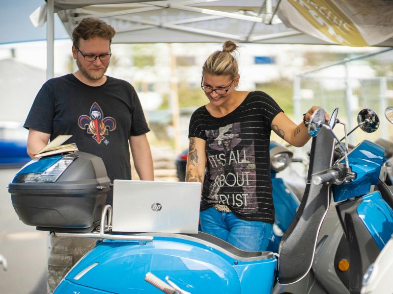 Two people look ta a laptop on a electronic scooter