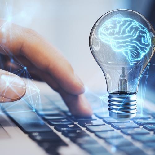 Hand typing on a computer with a brain icon in a lightbulb